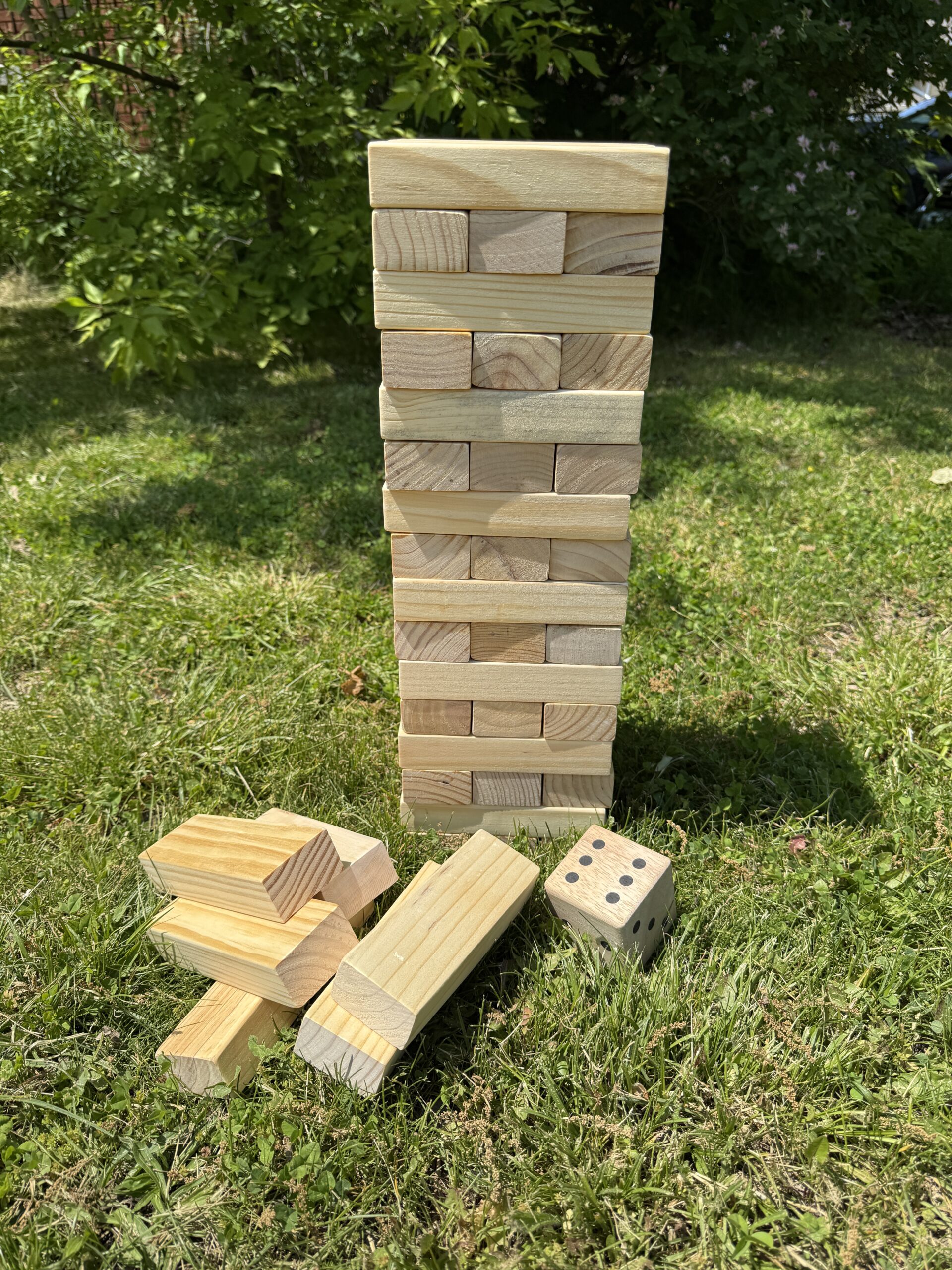 Jumbo Tumble Tower game - Wooden blocks stacked with a wooden dice sitting on the grass outside